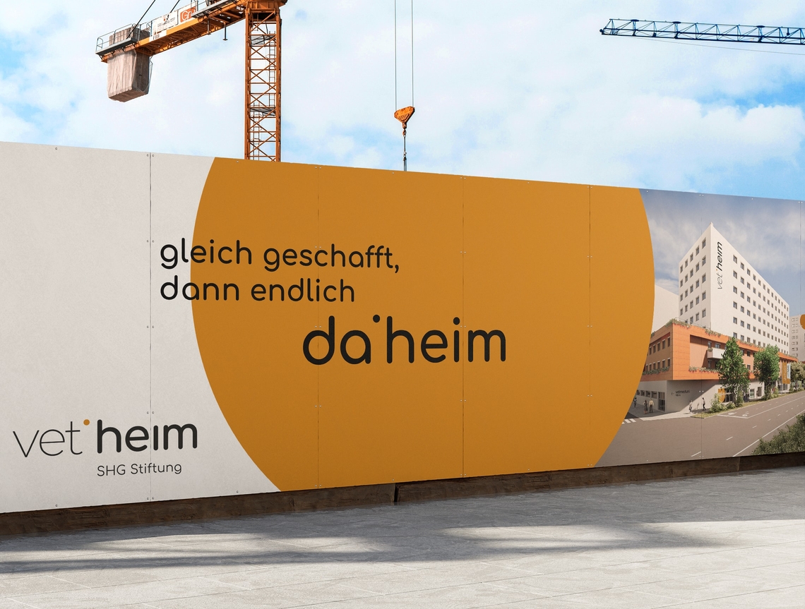 Bauzaun mit Ankündigung des neuen vetheim Hauses vor Baustelle
