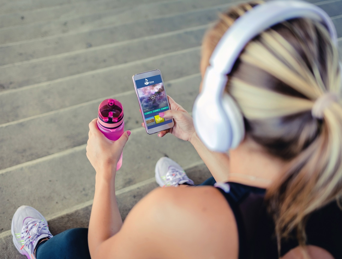 Junge, sportliche Frau mit Headphones sieht sich die freestream Website auf ihrem Handy an